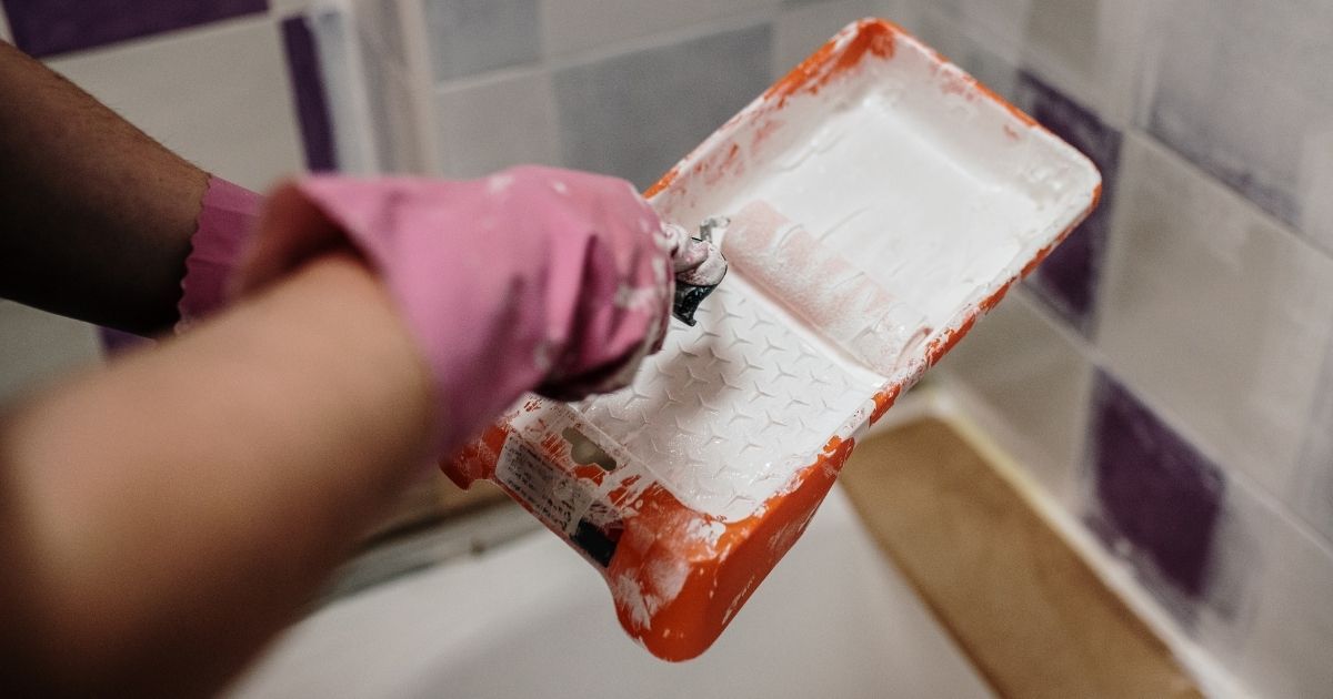 Mains d'un peintre qui repend le carrelage d'une salle de bain.