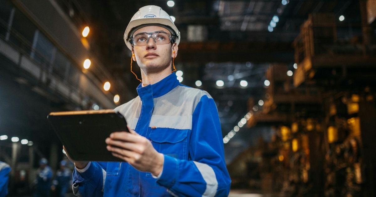 Ouvrier dans une industrie en train de vérifier les normes avec un casquede chantier et un feuillet.